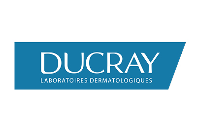 Ein blaues trapezförmiges Logo enthält das Wort „DUCRAY“ in großen weißen Buchstaben und darunter in kleineren weißen Buchstaben „LABORATOIRES DERMATOLOGIQUES“. Das Logo hat ein klares und modernes Design auf weißem Hintergrund.