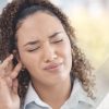 Frau fasst sich mit Finger ans Ohr. Ihr Gesicht ist verzogen. Zum Thema Was bedeutet Rauschen im Ohr