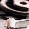 Nahaufnahme Löffel Kreatin mit Gewichten im Hintergrund