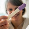 Glückliche Frau zeigt einen positiven Schwangerschaftstest in die Kamera zum Thema Nahrungsergänzungsmittel bei Kinderwunsch